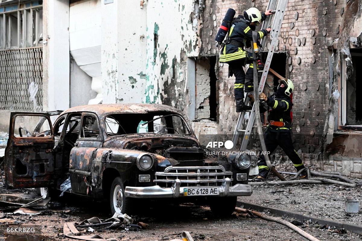 Firefighters are seen next to a burnt-out car following mass Russian drone and missile strikes in the western Ukrainian city of Lviv on July 12, 2025. - YURIY DYACHYSHYN / AFP