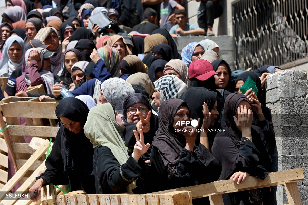 Palestinian women flash the V for victory sign as they line up to receive bags of flour at a UN World Food Programme (WFP) warehouse on Al-Jalaa street in Gaza City, in the central Gaza Strip on July 12, 2025. - AFP