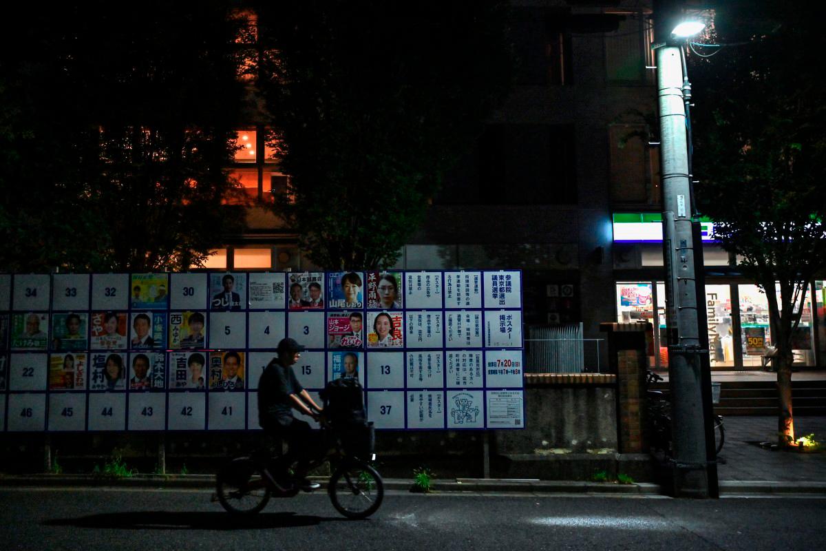 A man cycles past an election poster bulletin board showing different candidates in the upcoming July 20 upper house election, in central Tokyo on July 16, 2025. - AFP