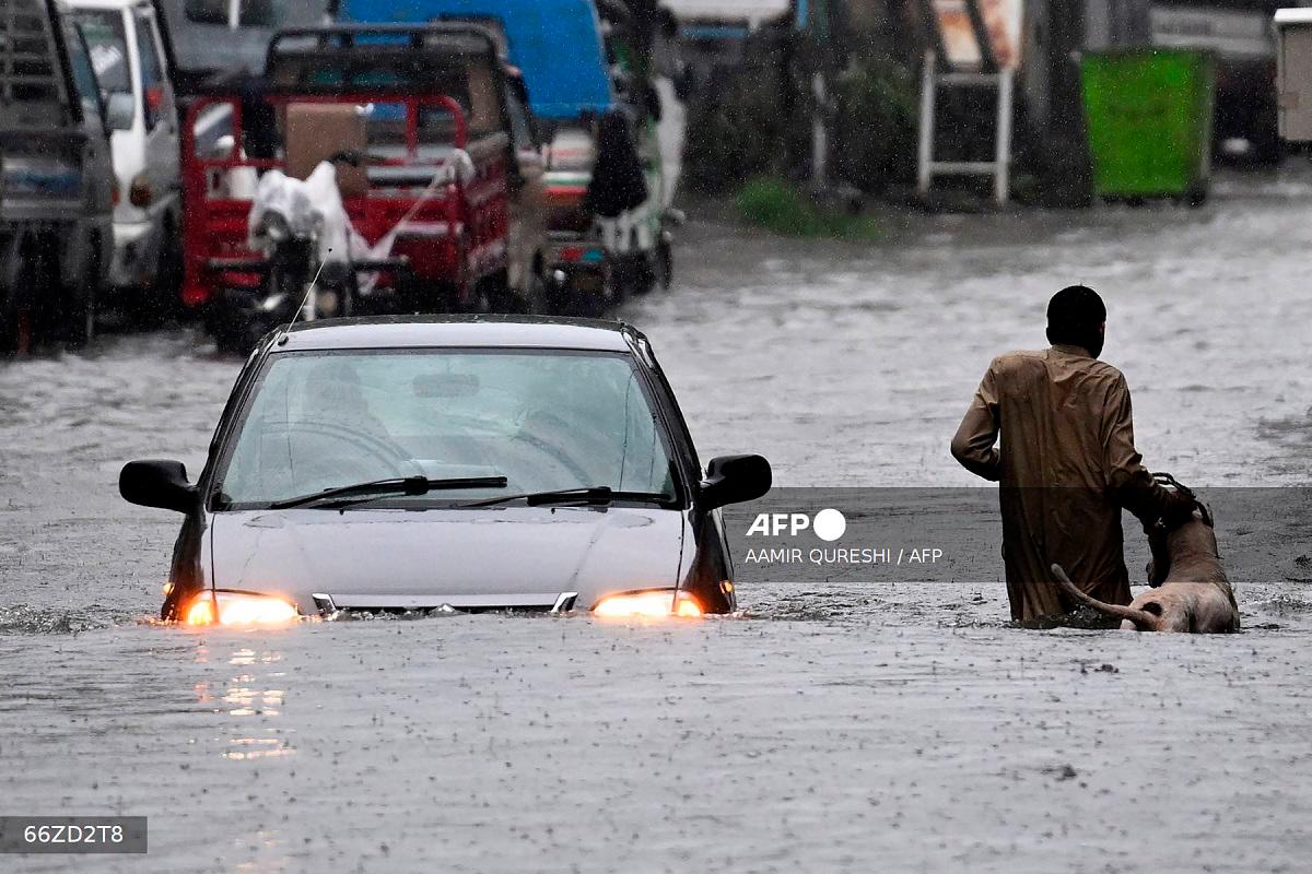A man along with his dog while a car wade through a flooded street during heavy monsoon rains in Rawalpindi on July 17, 2025. - Aamir QURESHI / AFP