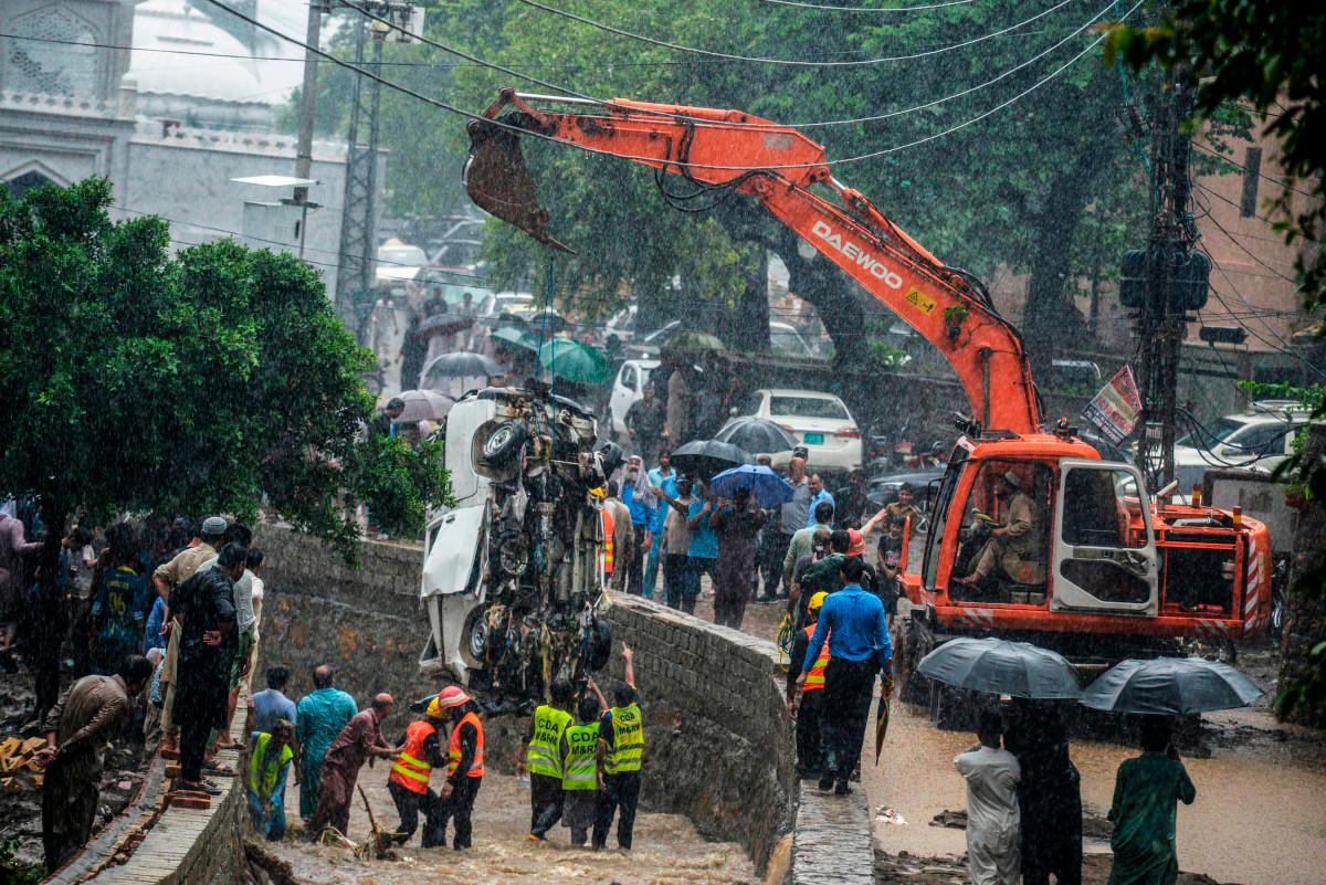 Rescuers and people look as a crane removes the wreckage of a van from a drainage after heavy monsoon rains in Islamabad on July 21, 2025. (Photo by M ASIM KHAN / AFP)