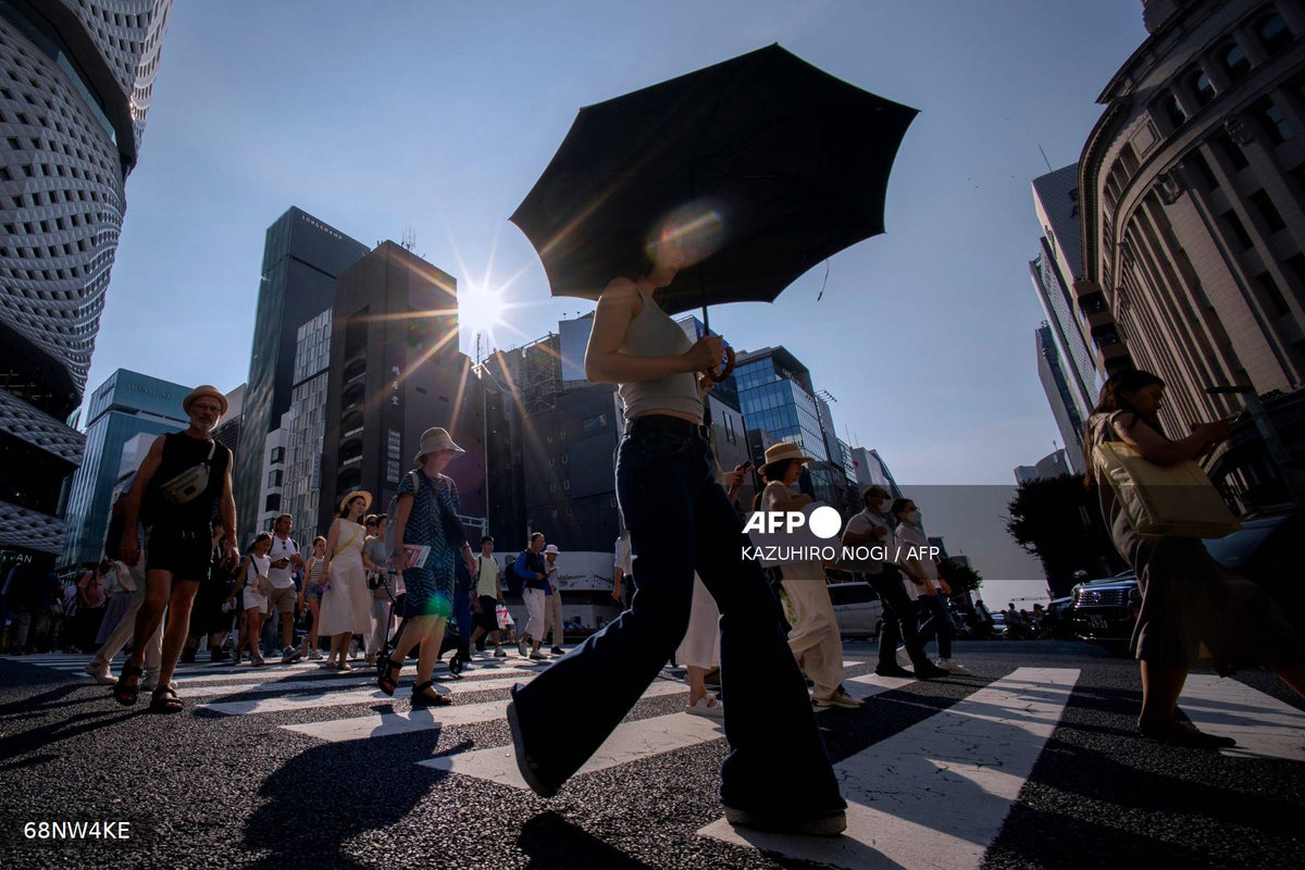 People cross a street on a hot day in Tokyo on August 4, 2025. - AFP