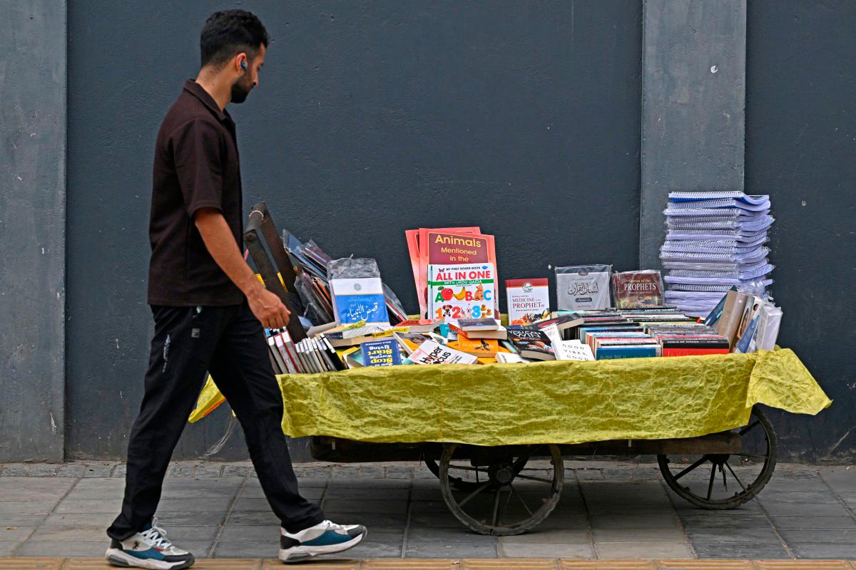 A pedestrian walks past a book cart along a roadside in Srinagar on August 7, 2025. (Photo by Tauseef MUSTAFA / AFP)