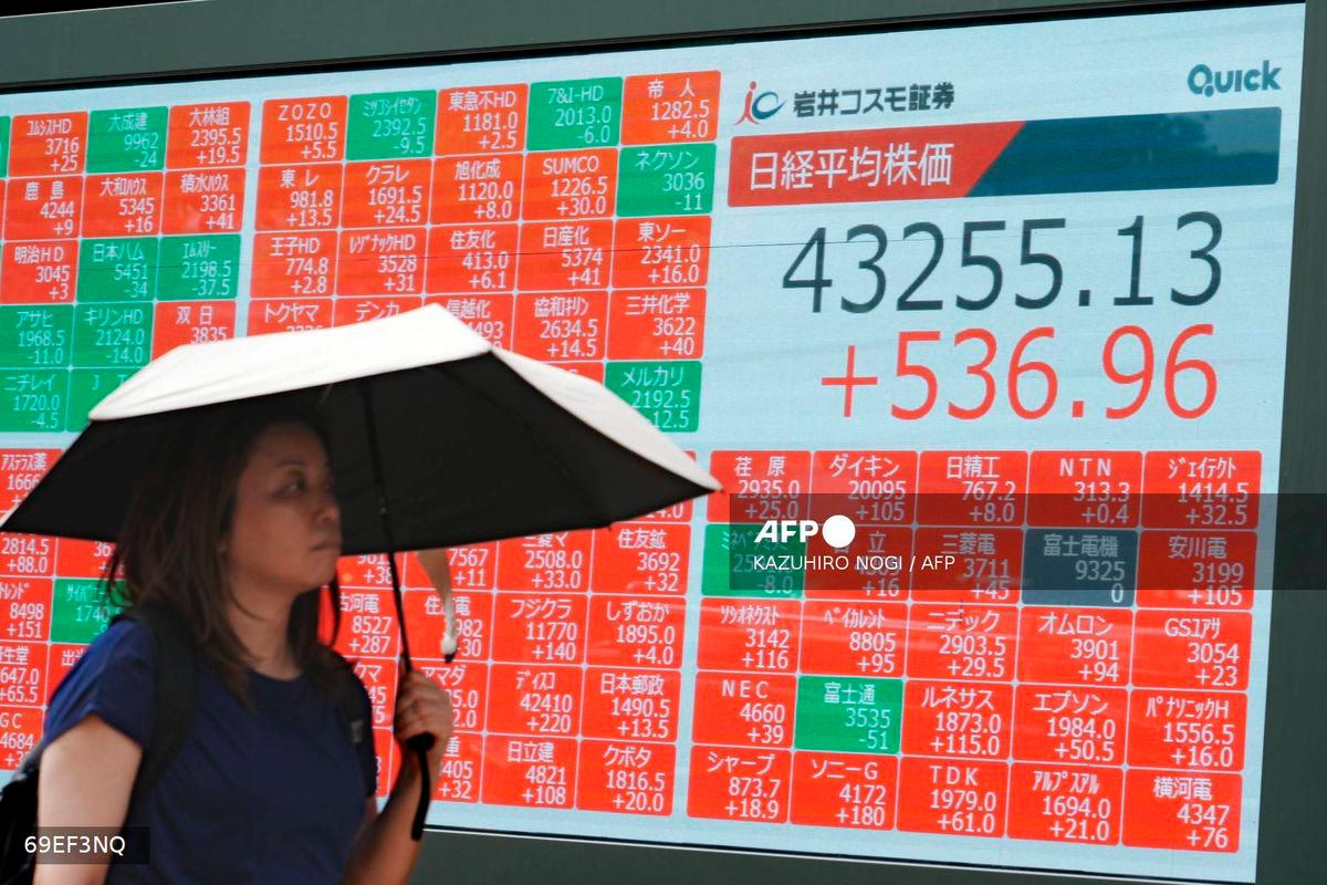 A woman walks in front of an electronic quotation board displaying the Nikkei Stock Average on the Tokyo Stock Exchange in Tokyo on August 13, 2025. (Photo by Kazuhiro NOGI / AFP)