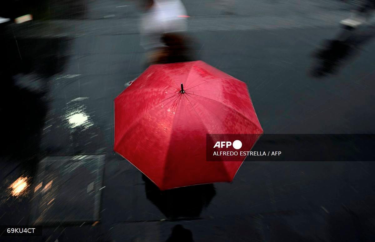 A person shelters under an umbrella from the rain in Mexico City on August 13, 2025. Mexico City has seen heavy rainfall since June 2025. - AFP
