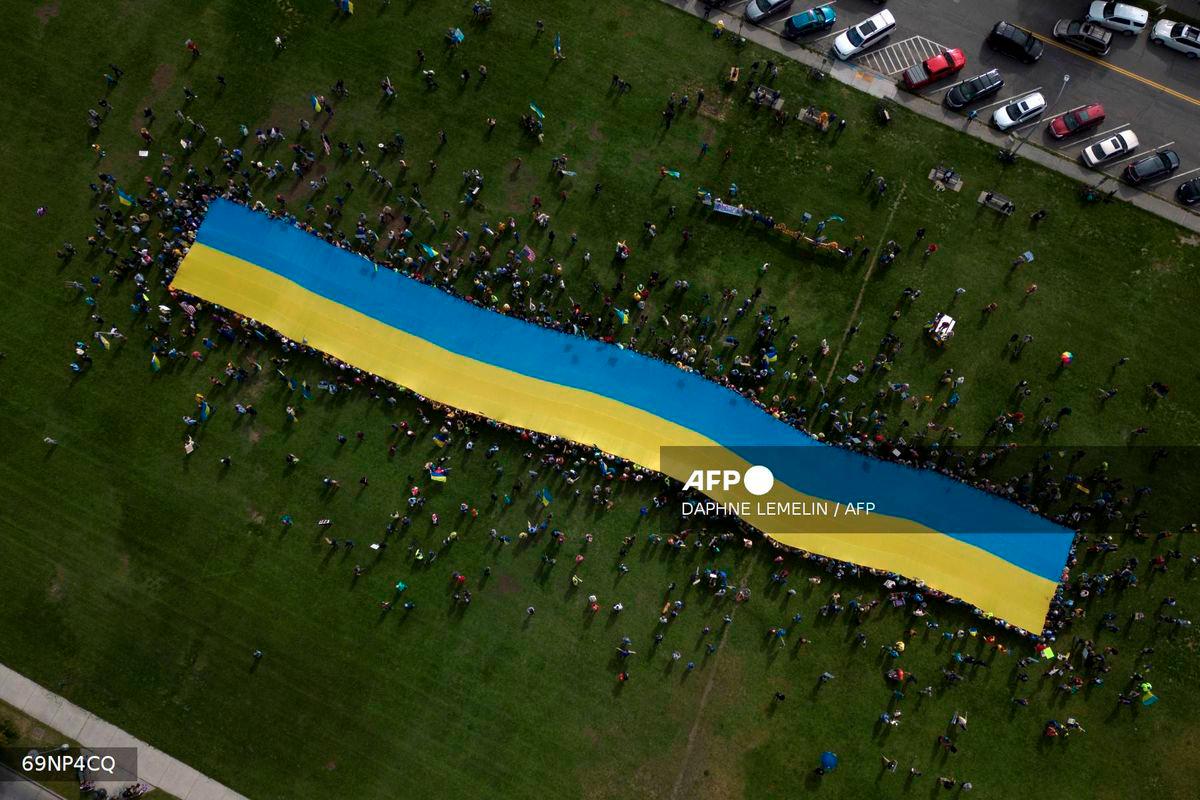 This aerial view shows protesters holding a giant Ukrainian flag in Anchorage, Alaska, on August 15, 2025 during a US-Russia summit at nearby Joint Base Elmendorf-Richardson. - AFP