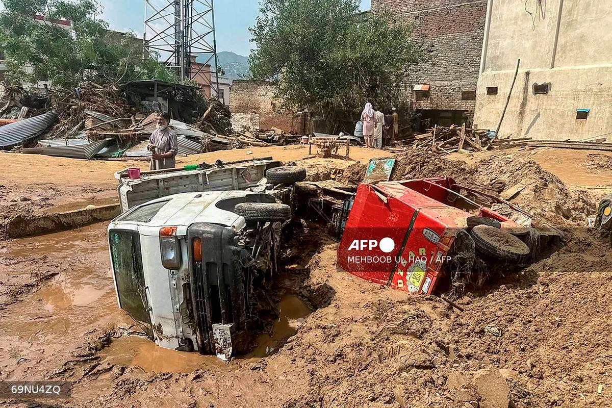 People walk past damaged vehicles and scattered debris after a road washed out following a flash flood in Mingora, the main city of Swat Valley, in monsoon-hit northern Pakistan's mountainous Khyber Pakhtunkhwa province on August 16, 2025. - AFP