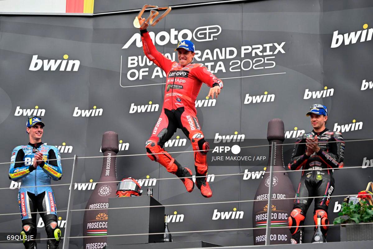 Winner Ducati Lenovo team's Spanish rider Marc Marquez (C) jumps on the podium as he celebrates next to second placed BK8 Gresini Racing MotoGP team's Spanish rider Fermin Aldeguer (L) and third placed Aprilia Racing team's Italian rider Marco Bezzecchi after the Austrian MotoGP Grand Prix at the Red Bull Ring race track in Spielberg, Austria, on August 17, 2025. - AFP
