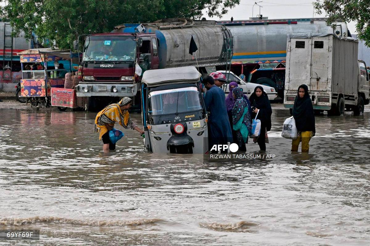 Passengers disembark from an auto rickshaw that got stranded on a flooded road after heavy monsoon rains in Karachi on August 20, 2025. (Photo by Rizwan TABASSUM / AFP)