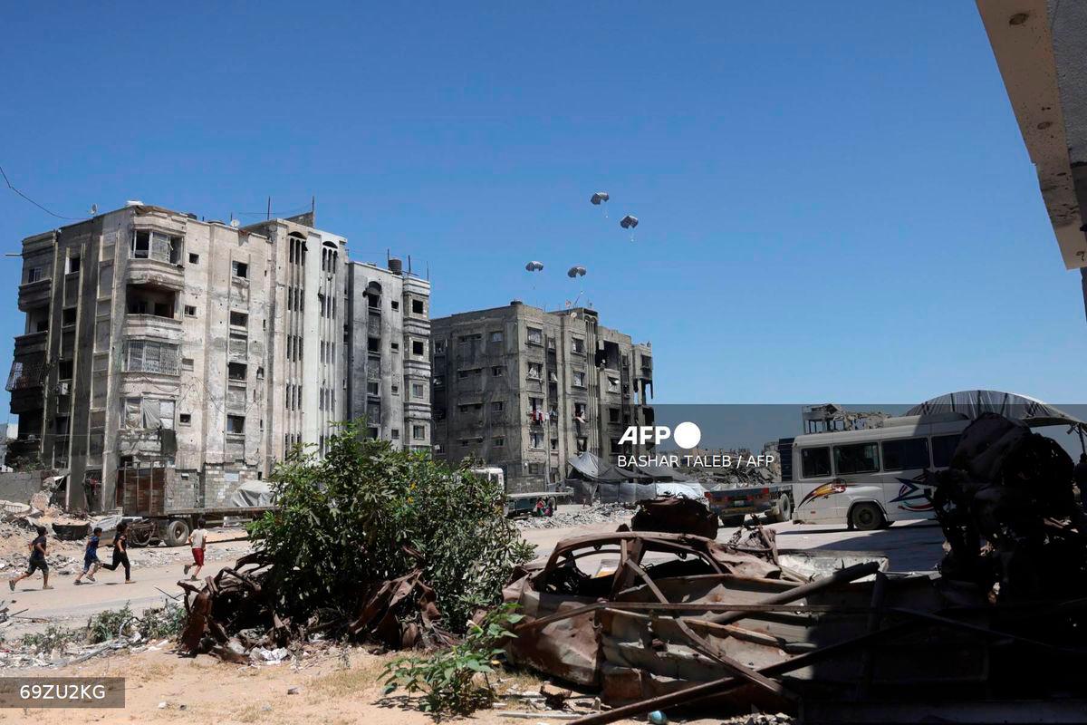 Palestinian run towards aid pallets as they parachute down after being dropped from a military plane near Jabalia in the northern Gaza Strip on August 20, 2025. - AFP