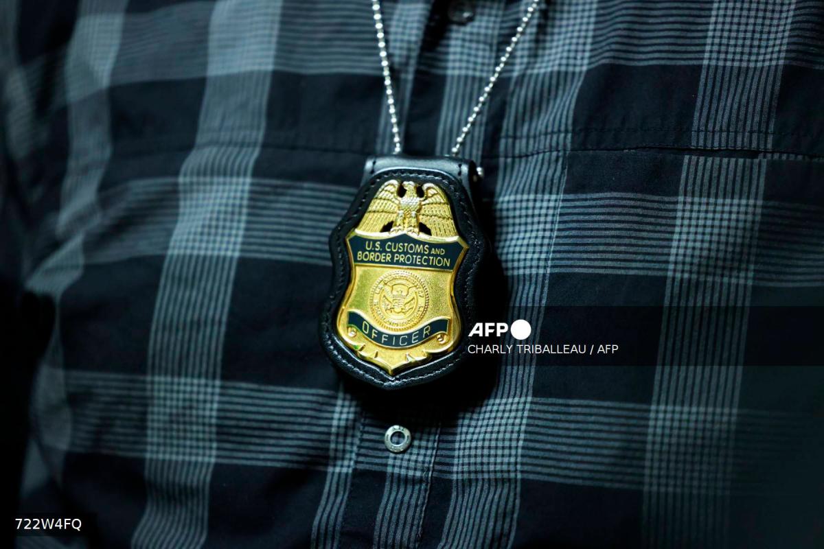 A federal agent’s badge hangs from his neck as he waits outside a courtroom at New York Federal Plaza Immigration Court in the Jacob K. Javits Federal Building, New York City, August 20, 2025. US President Donald Trump has made deporting undocumented immigrants a key priority for his second term, after successfully campaigning against an alleged “invasion” by criminals. (Photo by CHARLY TRIBALLEAU / AFP)