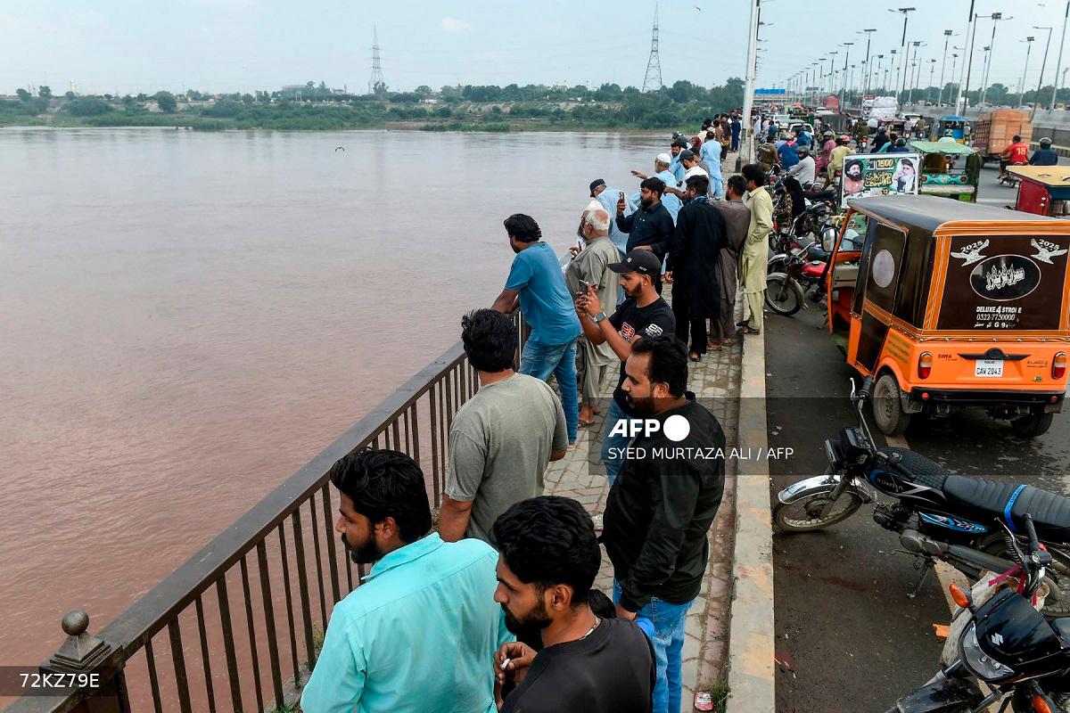 Commuters watch the Ravi River from a bridge as the government announced a flood alert in the riverside areas of Punjab province, in Lahore on August 27, 2025. - Syed Murtaza Ali / AFP