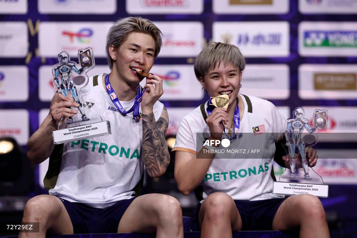 Malaysia’s Chen Tang Jie (L) and Toh Ee Wei hold their trophies as they bite their gold medals as they celebrate on the podium after beating China’s Jiang Zhen Bang and Wei Ya Xin in the mixed doubles final match at the Badminton BWF World Championships at the Adidas Arena in Paris, on August 31, 2025. - Thibaud MORITZ / AFP