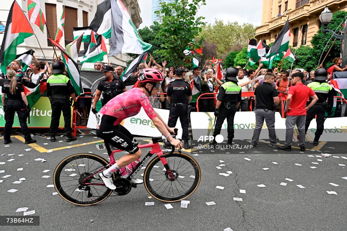 A cyclist competes as pro-Palestinian protesters holding Palestinian and Basque flags demonstrate during the eleventh stage of the Vuelta a Espana cycling tour, a 167 km race from Bilbao to Bilbao, on September 3, 2025. - AFP