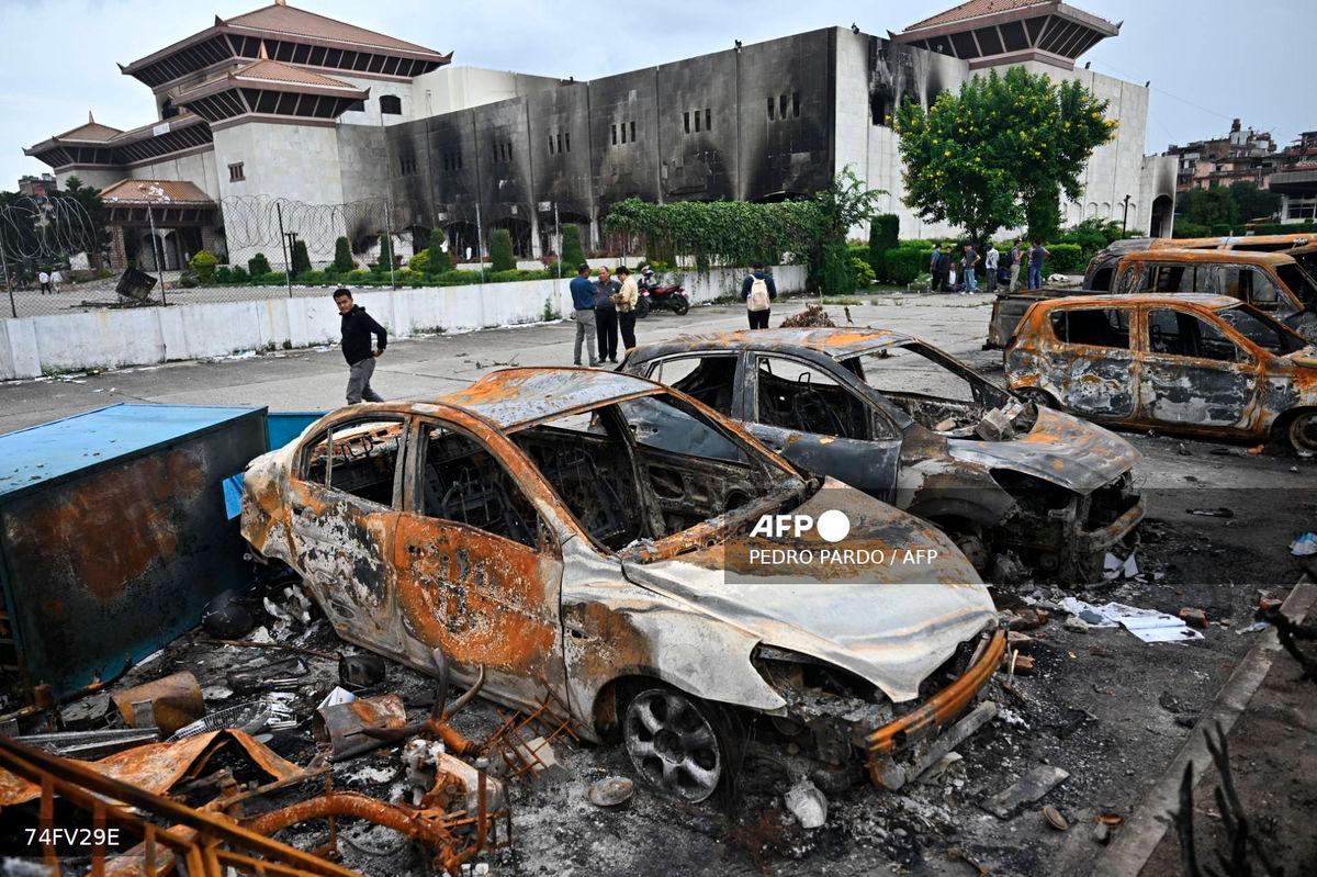 A man walks past the remains of charred vehicles at the parking lot of the torched Parliament building in Kathmandu on September 14, 2025. Nepal’s new leader Sushila Karki vowed on September 14, to follow protesters’ demands to “end corruption” as she began work as interim prime minister, after “Gen Z” youth demonstrations ousted her predecessor. (Photo by Pedro PARDO / AFP)