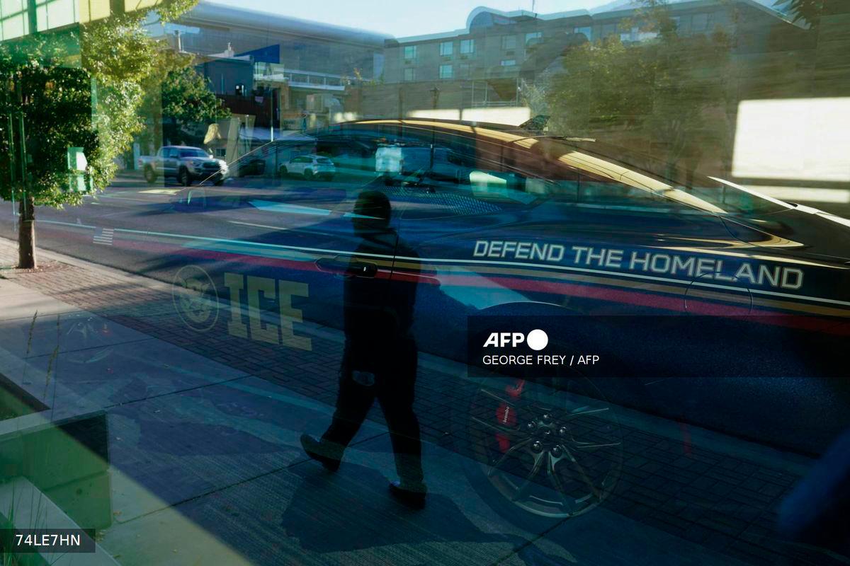 An ICE promotional car sits in a lobby as a man is reflected in a window as he walks to attend an ICE recruitment job fair at the Utah Valley Convention Center in Provo, Utah on September 15, 2025. - AFP