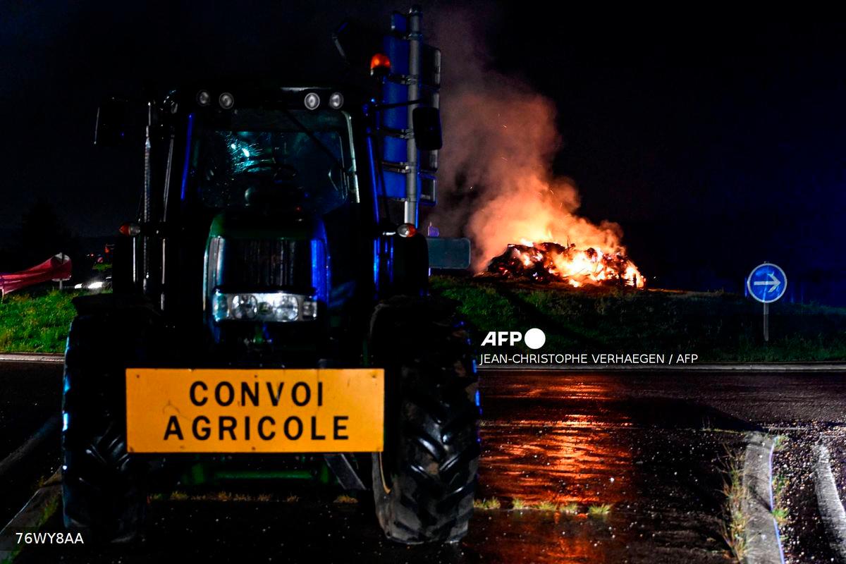 A tractor near a fire on a roundabout during a demonstration dubbed “Feux de la colere” (Fires of Wrath) called by French farmers’ union - (Photo by Jean-Christophe VERHAEGEN / AFP)