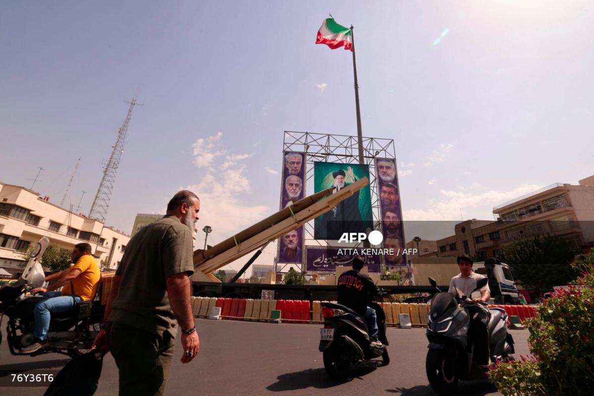 Iranians ride their motorcycles past a deactivated Kheibar Shekan ballistic missile in front of a picture of Iran's Supreme Leader Ayatollah Ali Khamenei in Tehran's Bahrestan Square on September 27, 2025, as part of an exhibit to mark the Sacred Defense Week commemorating the 1980-88 Iran-Iraq war. - AFPPIX