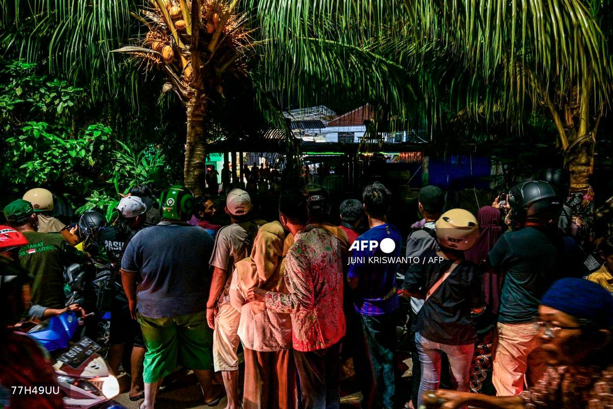 People gather to watch as a rescue operation is underway at the site of a collapsed building in a cordoned-off area at the Al Khoziny Islamic boarding school in Sidoarjo, East Java province, on October 2, 2025, after a multi-storey building at the school collapsed. - AFP