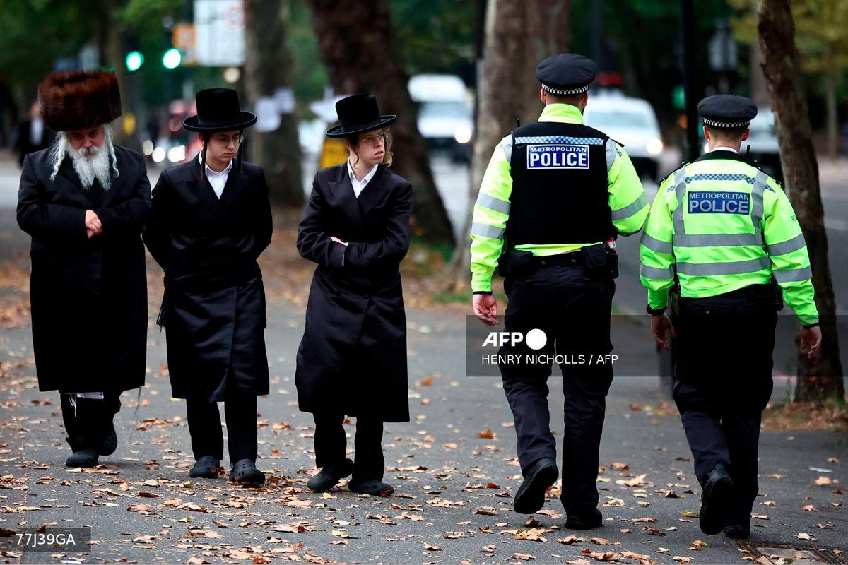 Members of the local Jewish community look on as police officers patrol the streets in Stanford Hill, north London on October 2, 2025. - AFP