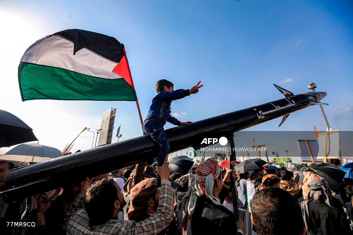 A boy sitting on a missile bearing the name Palestine gestures while next to him a man waves a Palestinian flag, during a rally by supporters of Yemen's Huthis condemning Israel and in support of Palestinians, near the Saleh Grand Mosque in the Huthi-held capital Sanaa on October 3, 2025. - AFP