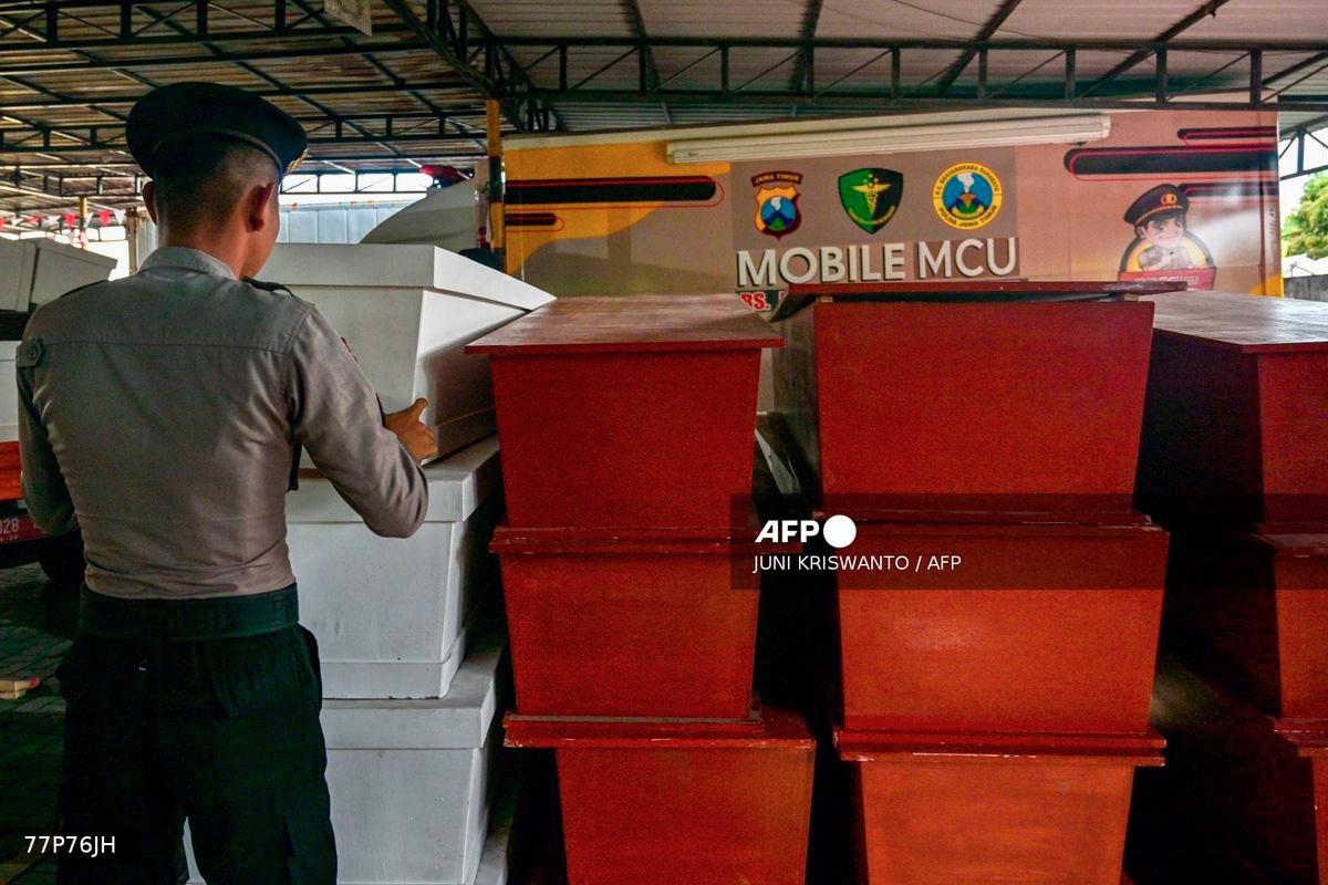 A Police officer stacks coffins for victims of a building collapse at the Al Khoziny Islamic boarding school, at the Bhayangkara hospital in Surabaya, East Java province on October 4, 2025. - AFP