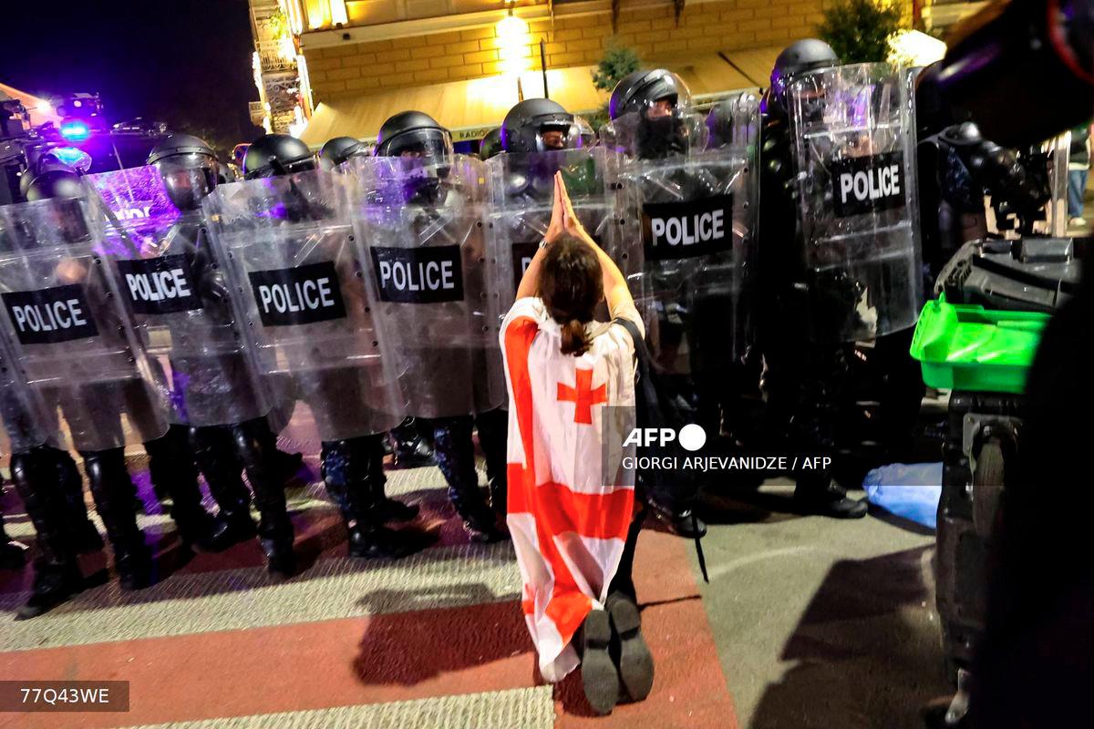 A protester wrapped in a Georgian flag gestures in front of riot police during an opposition rally on the day of local elections in central Tbilisi on October 4, 2025. - AFP