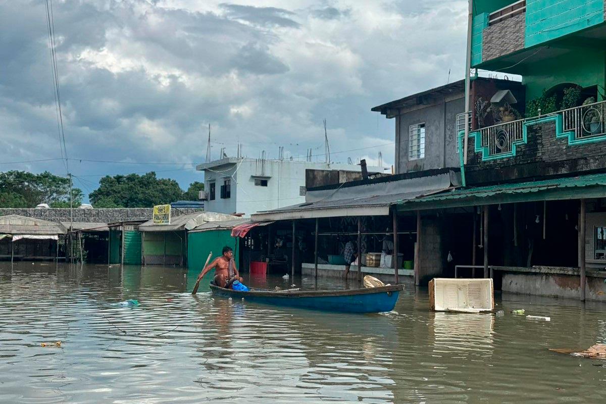 This photo taken on October 4, 2025 shows a resident paddling a wooden boat past flooded houses near an inundated river after a dam released waters due to heavy rains brought by Tropical Storm Matmo in Tuguegarao City. - John Dimain / AFP