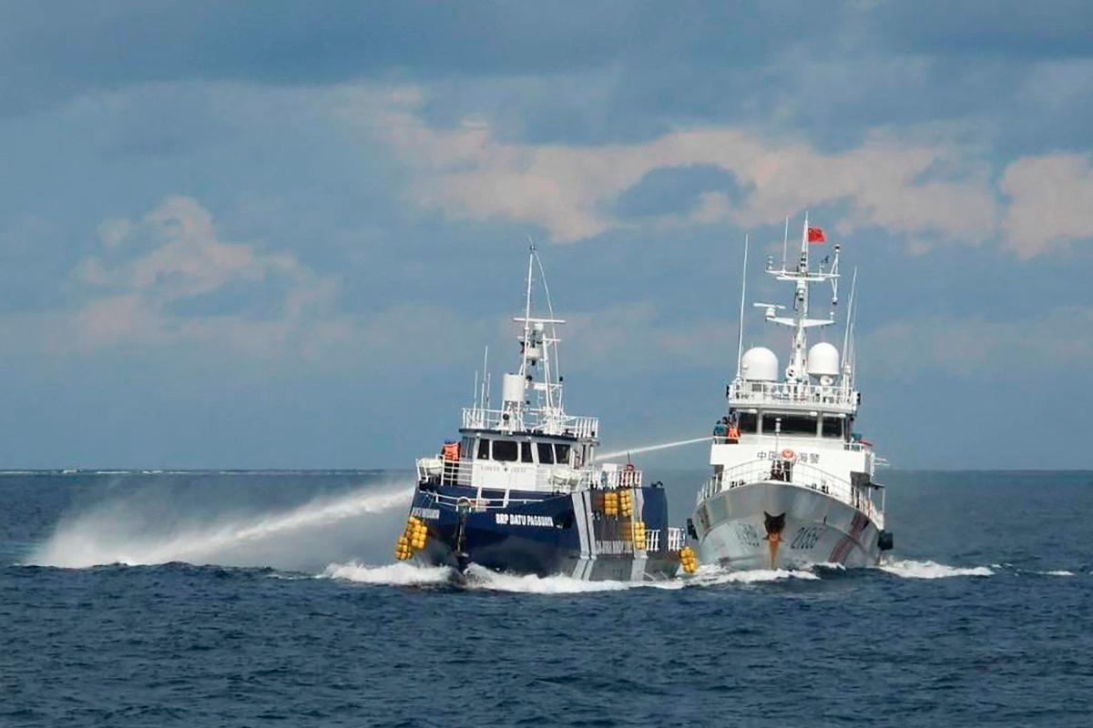 This handout photo taken and released on October 12, 2025 by the Philippine Coast Guard shows a China Coast Guard ship (R) deploying water cannon as a Philippine Bureau of Fisheries vessel (L) is seen alongside during an incident near Thitu island in disputed waters of the South China Sea. - AFP/ PHILIPPINE COAST GUARD
