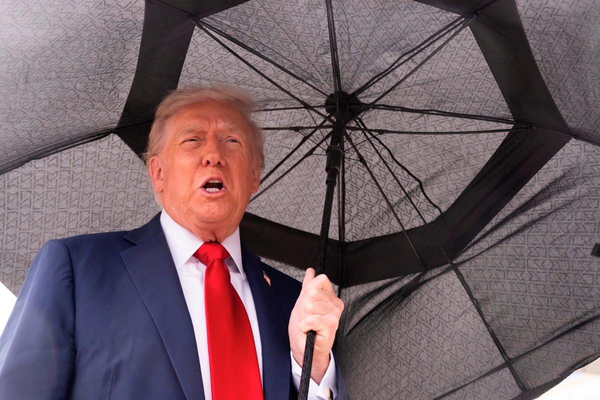 US President Donald Trump holds an umbrella as he speaks to reporters before boarding Air Force One prior to departure from Joint Base Andrews in Maryland, October 12, 2025. - AFP