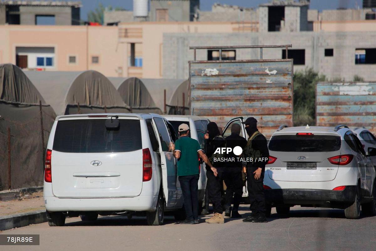 Members of Hamas military wing, Al-Qassam Brigades, stand guard next to vehicles carrying released Israeli hostages on a main road in Deir al-Balah in the central Gaza Strip on October 13, 2025. Hamas has handed over the first seven of 20 surviving Israeli hostages to Red Cross representatives in Gaza City, Israeli public radio reported on October 13. - AFP