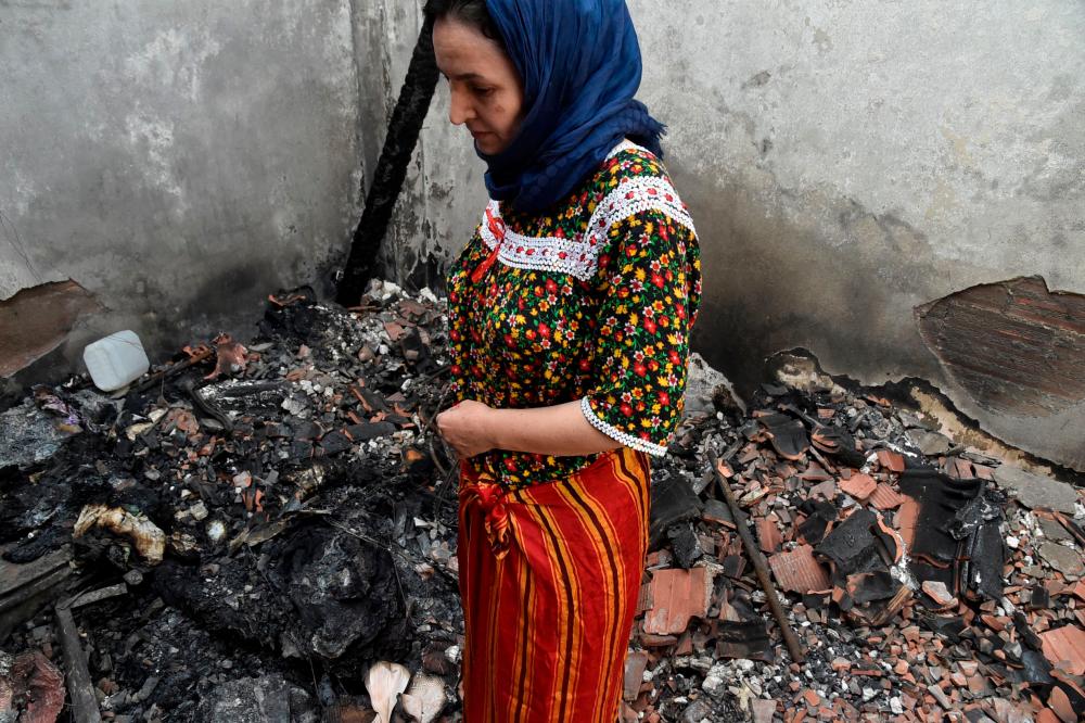 An Algerian woman dressed in a traditional outfit stands amidst the charred debris of her home that burned down during wildfires in the Ait Daoud area of northern Algeria, on August 13, 2021. -AFP
