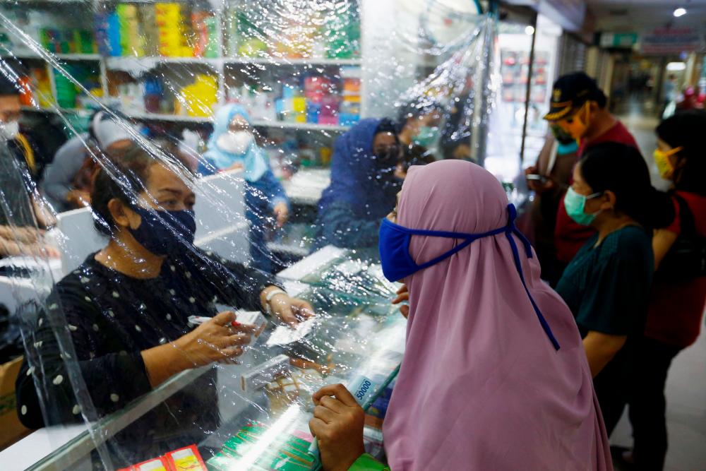 Customers wearing protective face masks make their transactions through a plastic barrier as a preventive measure against the coronavirus disease (Covid-19) in Jakarta, Indonesia, April 2. - Reuters