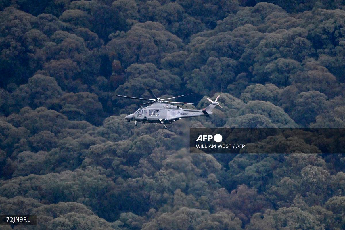 A Victoria police helicopter circles the peaks as the search intensifies for a fugitive linked to the cold-blooded murder of two police officers in Porepunkah on August 27, 2025. Police searched the Australian bush on August 27, for a heavily armed 56-year-old gunman still on the run a day after allegedly killing two officers and wounding a third. - WILLIAM WEST / AFP