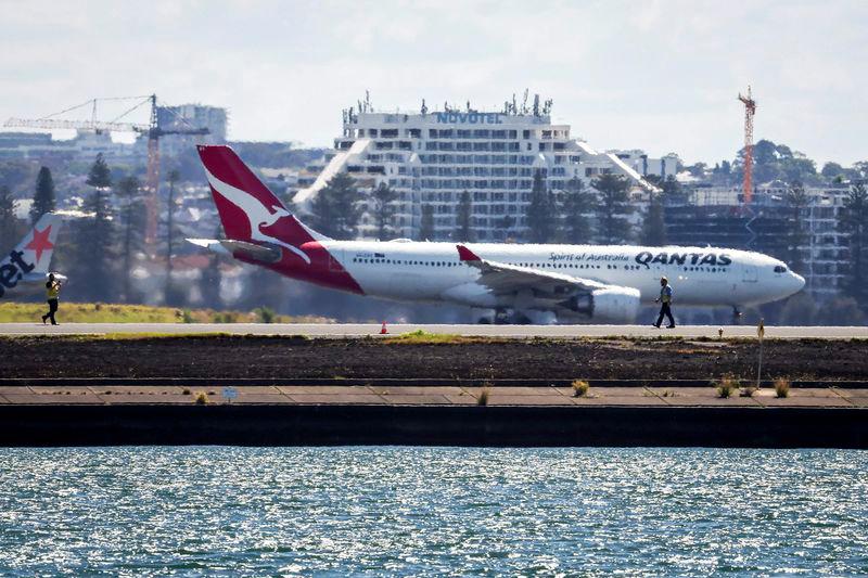 Workers check the runway as a Qantas plane prepares to take off behind them at Sydney International Airport on November 8, 2024. - AFPPIX