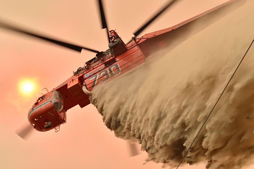 A helicopter drops fire retardent to protect a property in Balmoral, 150km southwest of Sydney on Dec 19. — AFP