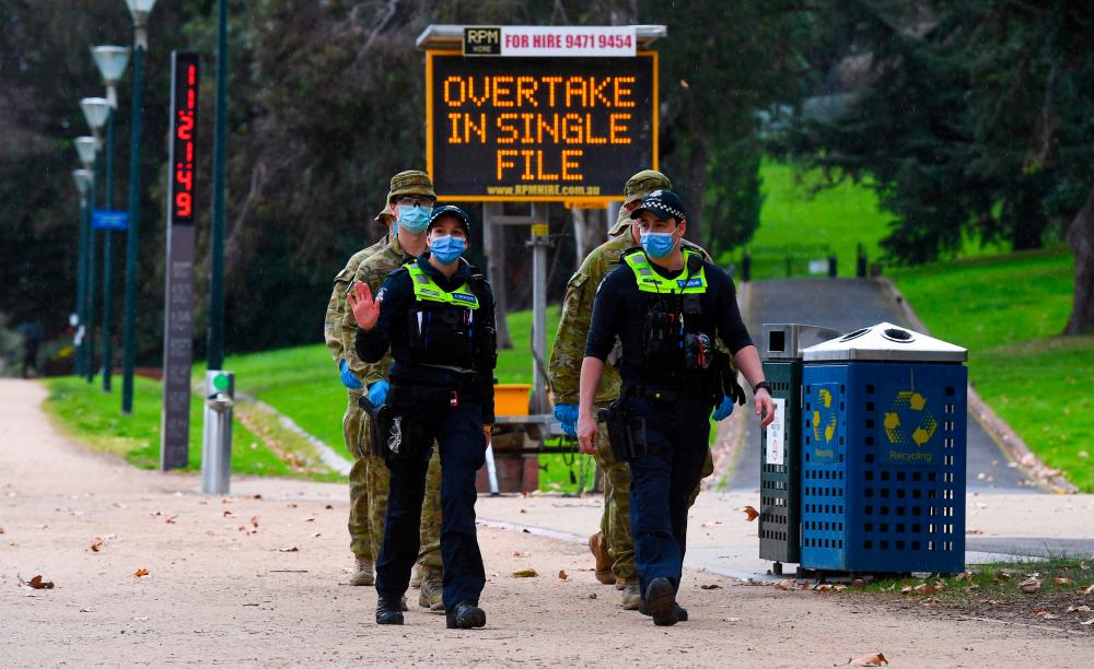 Police officers and soldiers patrol a popular running track in Melbourne on Aug 4, 2020 after the state announced new restrictions as the city battles fresh outbreaks of the Covid-19 coronavirus. — AFP