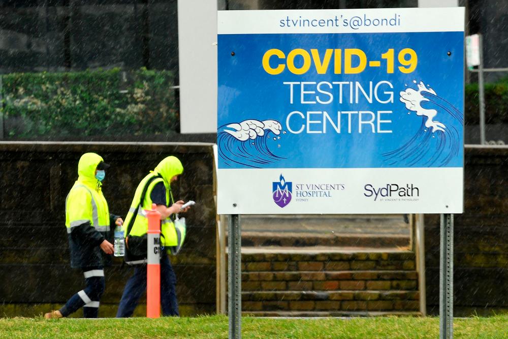 Medical officers walk past a sign board of Covid-19 testing center on Bondi Beach in Sydney on May 6, 2021, as administration implementing new restrictions after new cases of community transmission. –AFP