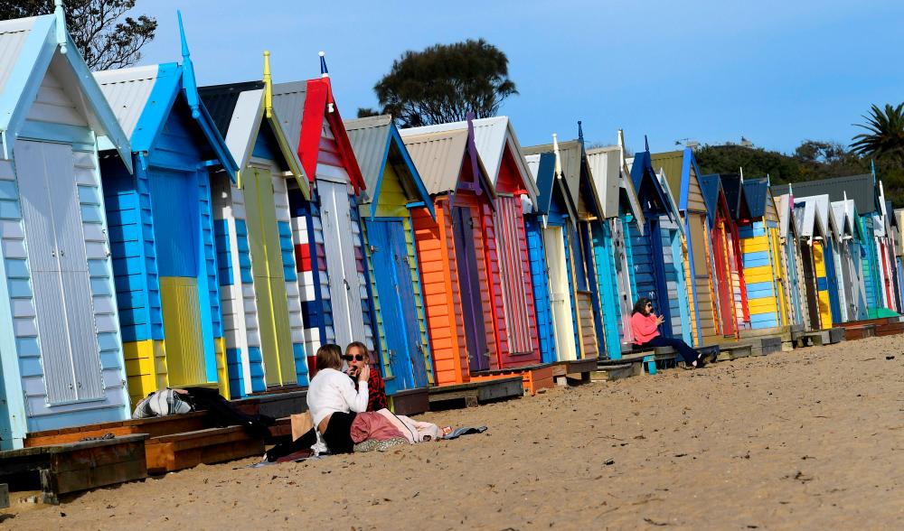 People enjoy a mid-winter picnic in front off the Brighton bathing boxes in Melbourne on June 22, 2021 as the city's latest Covid-19 outbreak recedes while Sydney battles a fresh cluster, highlighting Australia's difficulty in quashing persistent small virus flare-ups. – AFP