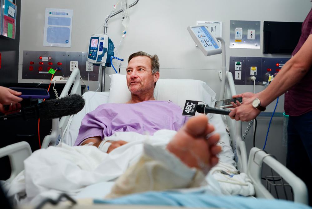 This handout photo received from Princess Alexandra Hospital in Brisbane on September 18, 2019 shows Neil Parker, 54, an Australian bushwalker talking to the media from his hospital bed after he tumbled down a waterfall, snapping his leg in two, and managing to crawl for two arduous days though scrub and forest to safety. — AFP