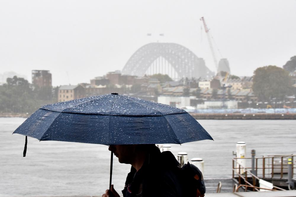 A man walks in front of the Harbour Bridge during rainfall in Sydney on April 7, 2022, as inclement weather triggered evacuation orders in several suburbs of Sydney’s south and southwest. AFPPIX