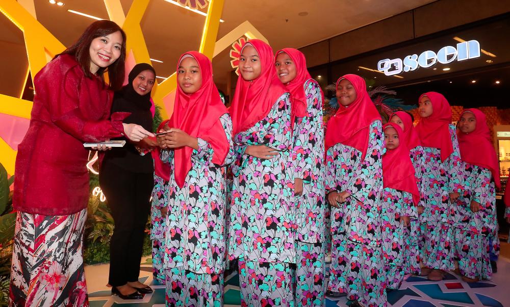Too (left) hands out “Duit Raya” packets to the children. SUNPIX by MASRY CHE ANI