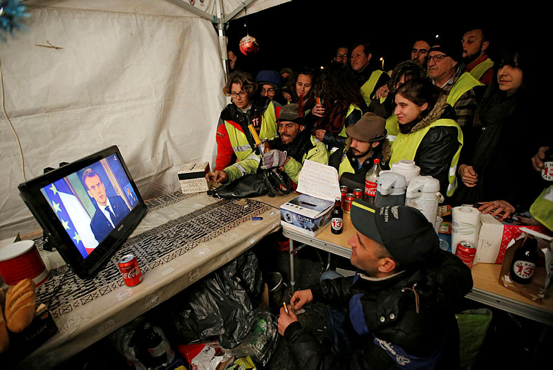 Protesters wearing yellow vests watch French President Emmanuel Macron on a TV screen at the motorway toll booth in La Ciotat, near Marseille, France, Dec 10, 2018. — Reuters