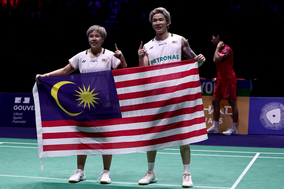 Chen Tang Jie and Toh Ee Wei (L) hold their national flag as they celebrate beating China’s Jiang Zhen Bang and Wei Ya Xin in the mixed doubles final match at the Badminton BWF World Championships at the Adidas Arena in Paris, on August 31, 2025. - Thibaud MORITZ / AFP