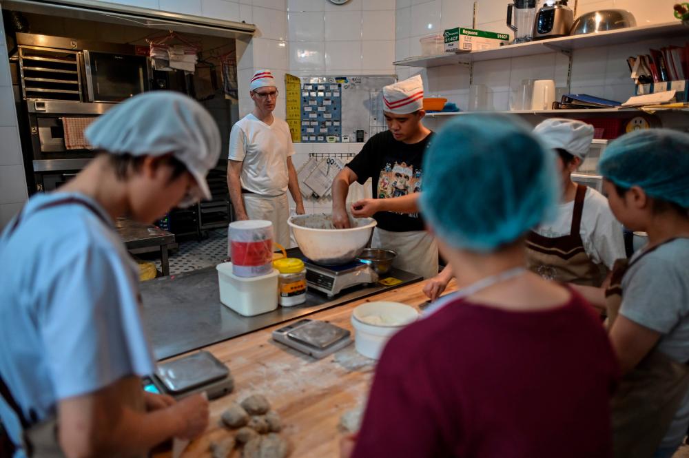 This photo shows Uwe Brutzer (back L) working with hearing-impaired employees at his bakery in the city of Changsha in China's Hunan province. The oven's warm glow and aroma of fresh bread signal the morning rush at Bach's Bakery in the central Chinese city of Changsha, but although the baking staff chatter excitedly, you could hear a pin drop. / AFP / Hector RETAMAL