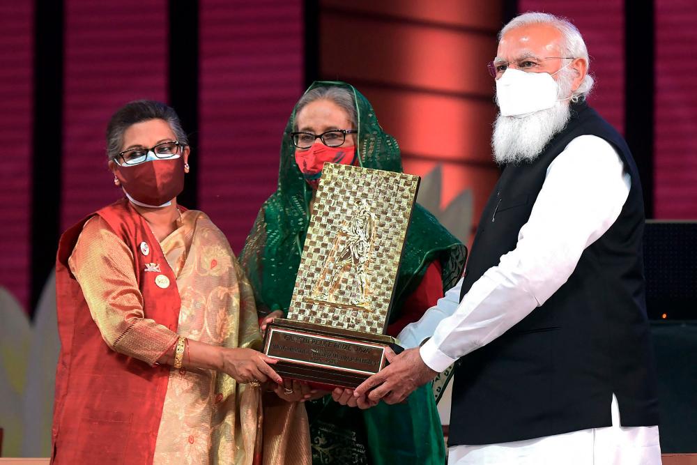 In this handout photo released by Bangladesh Prime Minister Office and taken on March 26, 2021 Indian Prime Minister Narendra Modi (R) hands over the Gandhi Peace Prize given posthumously to the late Bangladesh’s founder Sheikh Mujibur Rahman to his daughters Bangladesh’s Prime Minister Sheikh Hasina (C) and Sheikh Rehana, in Dhaka. - AFP