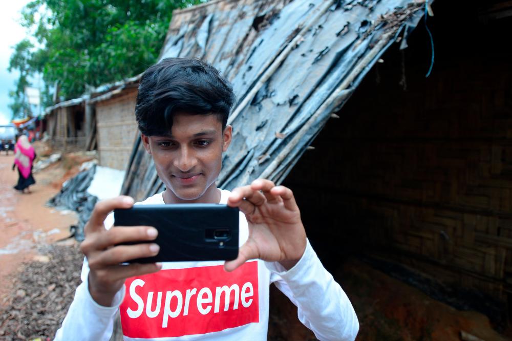 In this picture taken on July 23, 2019, Rohingya youth Mohammad Rafiq uses his mobile phone to take photos at the Kutupalong refugee camp. — AFP