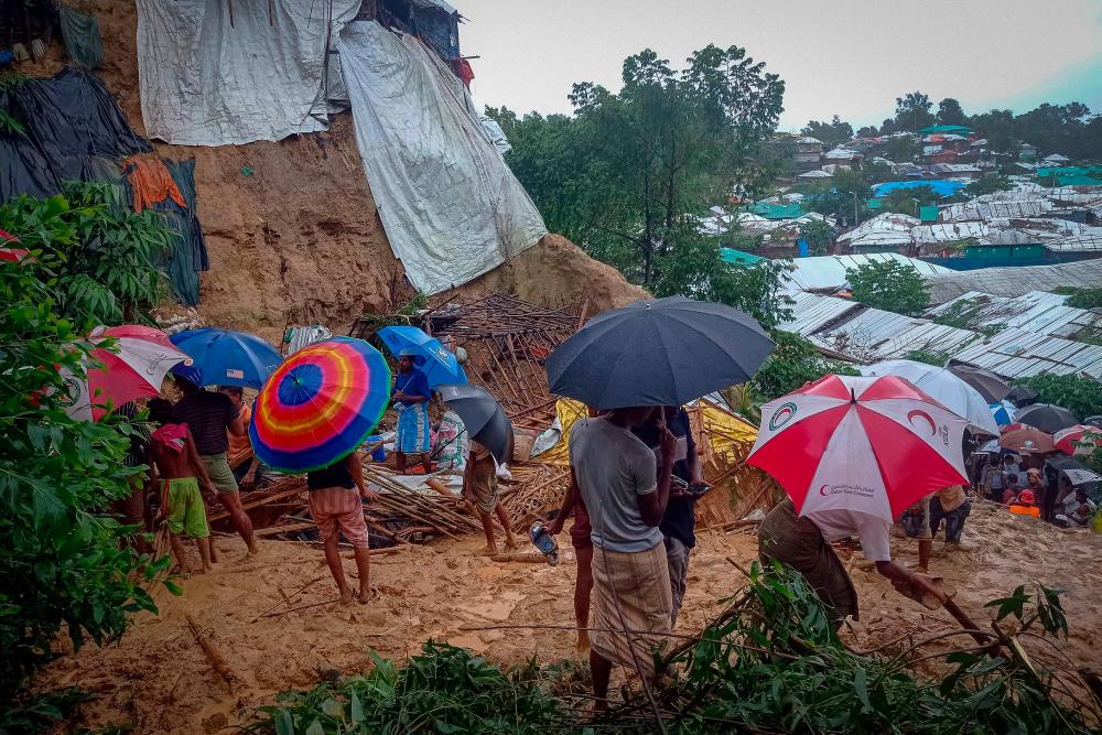 Onlookers stand as Rohingya refugees work amid the debris of houses in Balukhali camp on July 27, 2021 that were damaged after monsoon rains triggered landslides and flash floods in the hilly settlements killing at least six. -AFP