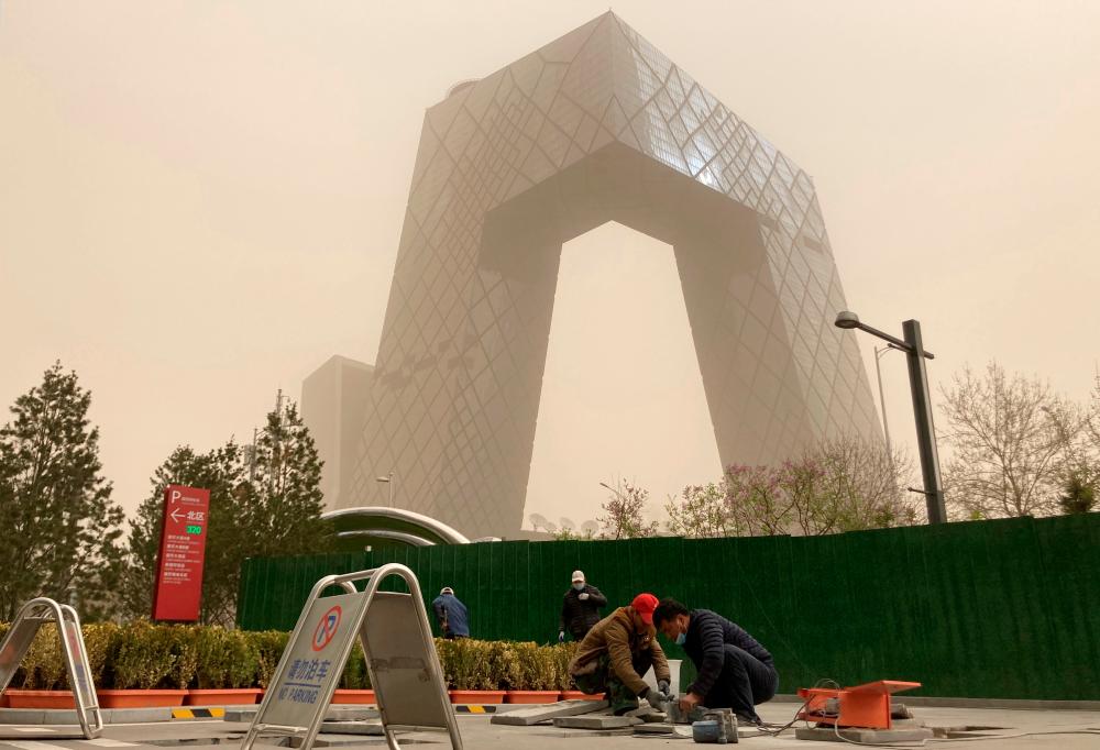 Construction workers are seen in front of the CCTV headquarters shrouded in dust as the city is hit by a sandstorm, in Beijing, China March 28, 2021. — Reuters