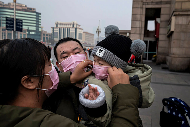 A mother (L) of a child (R) held by his father (C) adjust his protective mask to help stop the spread of a deadly virus which began in Wuhan peaks through a plastic curtain at the Beijing railway station in Beijing on Jan 27, 2020. — AFP